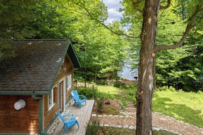 Une cabane au revêtement extérieur en bois, une véranda avec des chaises bleues et une vue sur un lac entouré d’arbres.