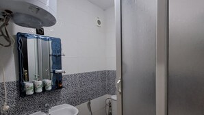 Un baño con lavamanos blanco, inodoro y ducha. Hay un espejo sobre el lavamanos y un perchero.