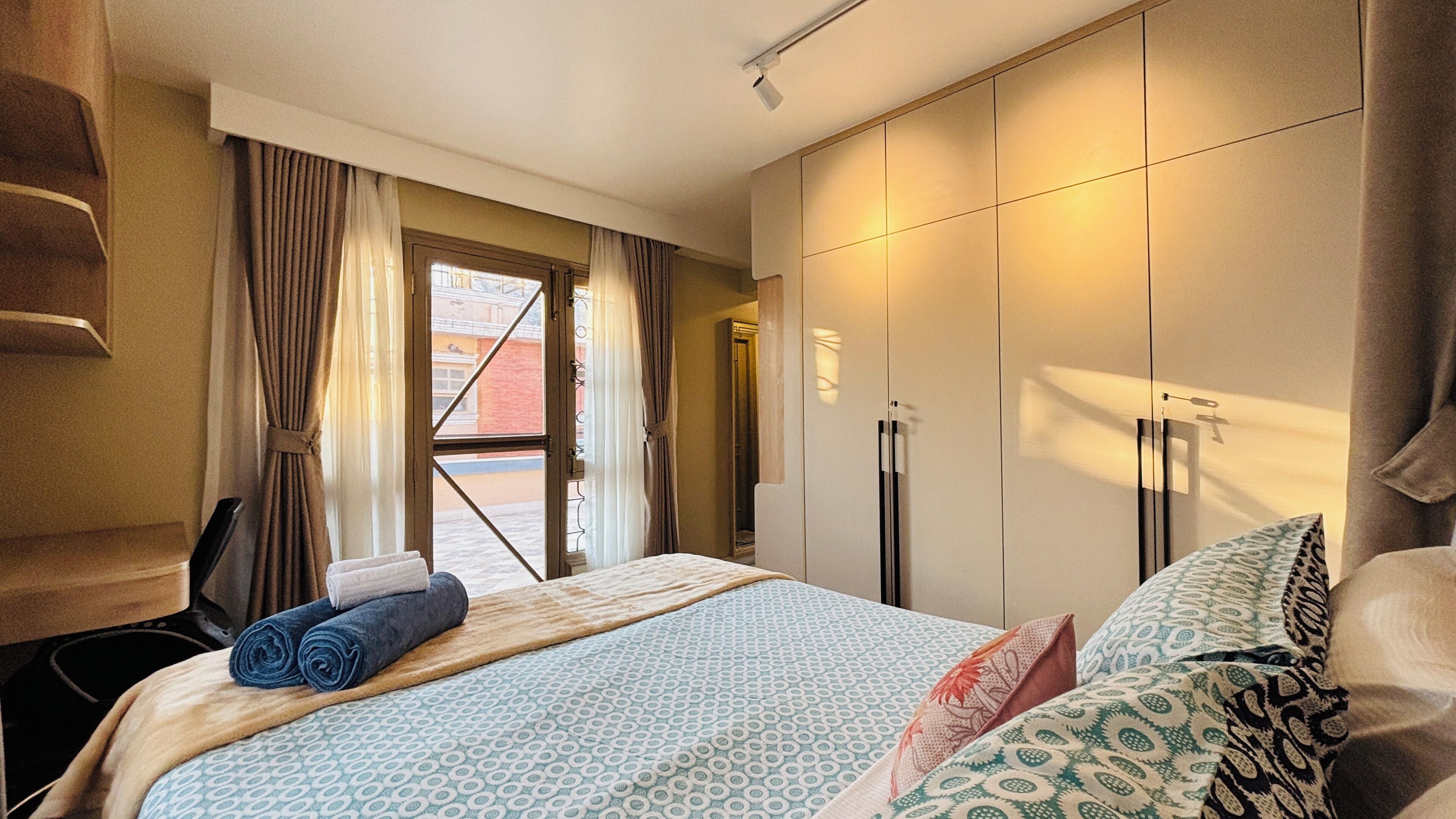 A hotel room with a bed, a wardrobe, a desk, and a window with curtains.