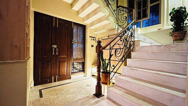 A staircase with a wooden handrail and a metal balustrade, leading to a landing with a dark wooden door and a potted plant. - Spacious 2BR Home Near Patan with Himalayan Views (Lalitpur)