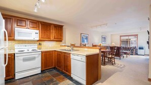 A kitchen with wooden cabinets, a microwave, stove, and dishwasher. There is a dining area with a table and chairs. - Powderhorn Suite-Ski/Out, Hot Tub w/ Mountain View (Brighton)