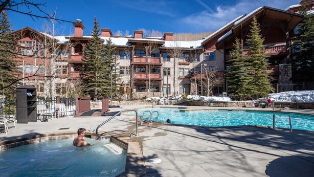 A pool area with a hot tub, surrounded by multi-story buildings with balconies and a snowy landscape. - Powderhorn Suite-Ski/Out, Hot Tub w/ Mountain View (Brighton)