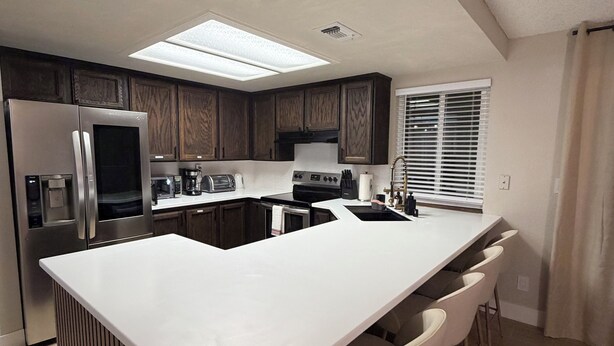A modern kitchen with a central island, bar stools, a refrigerator, a stove, and a microwave. - Spacious 4-bedroom house with AC in charming Roseville (Roseville)