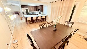 A dining area with a wooden table and chairs, a vase with flowers, and a kitchen in the background. - Spacious 4-bedroom house with AC in charming Roseville (Roseville)