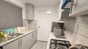 Une cuisine de taille réduite, équipée d’une cuisinière à gaz, d’un évier et de placards.
