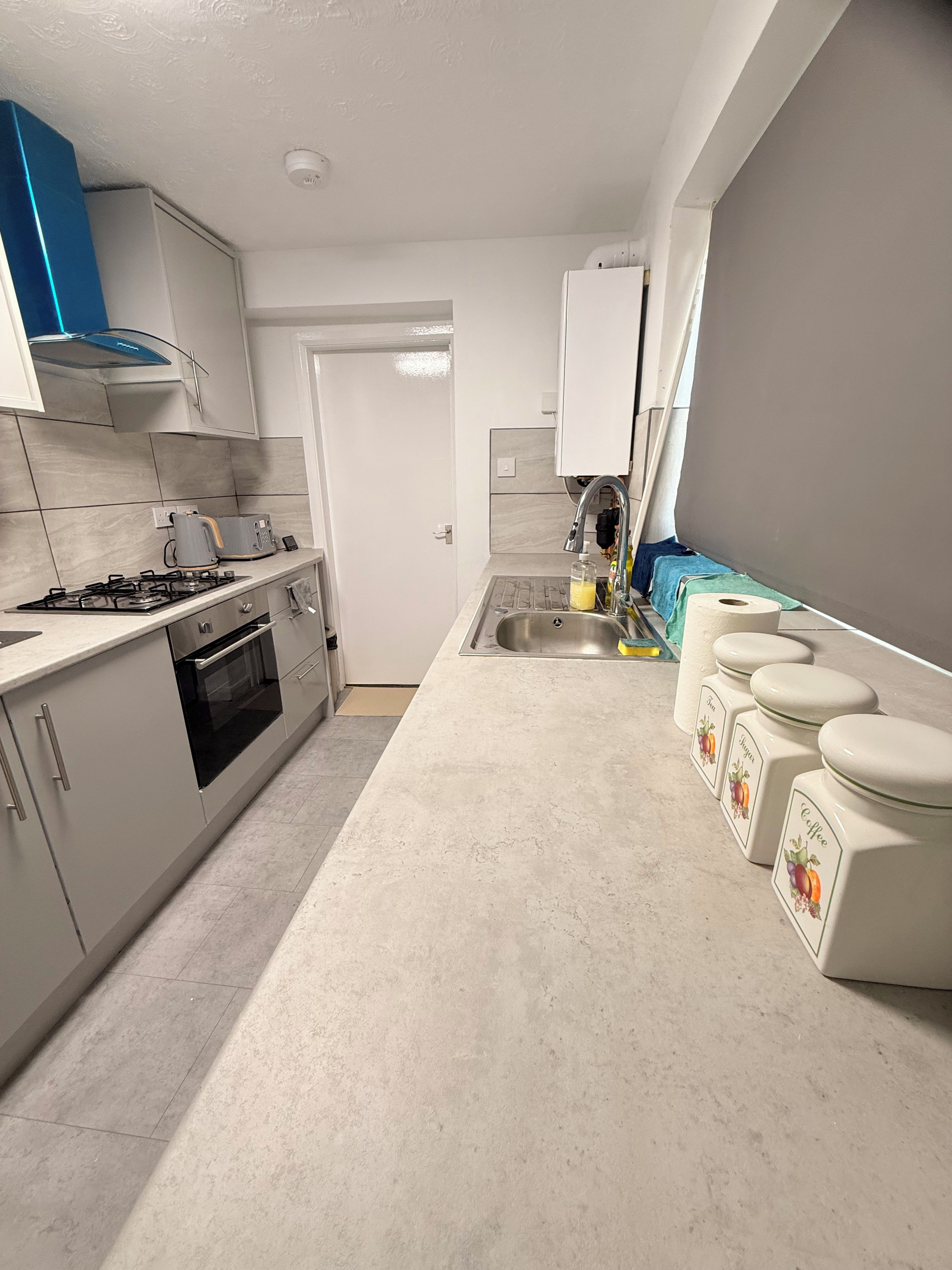 A modern kitchen with a gas stove, oven, and a sink. There are cabinets and a blue range hood.