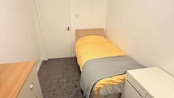 A bedroom with a bed, a dresser, a desk, and a door.