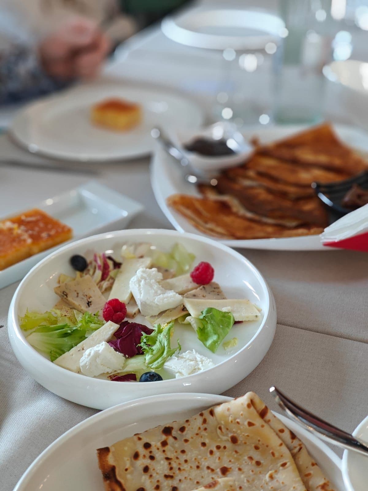 A dining table with various dishes including a salad, cheese, and flatbreads.