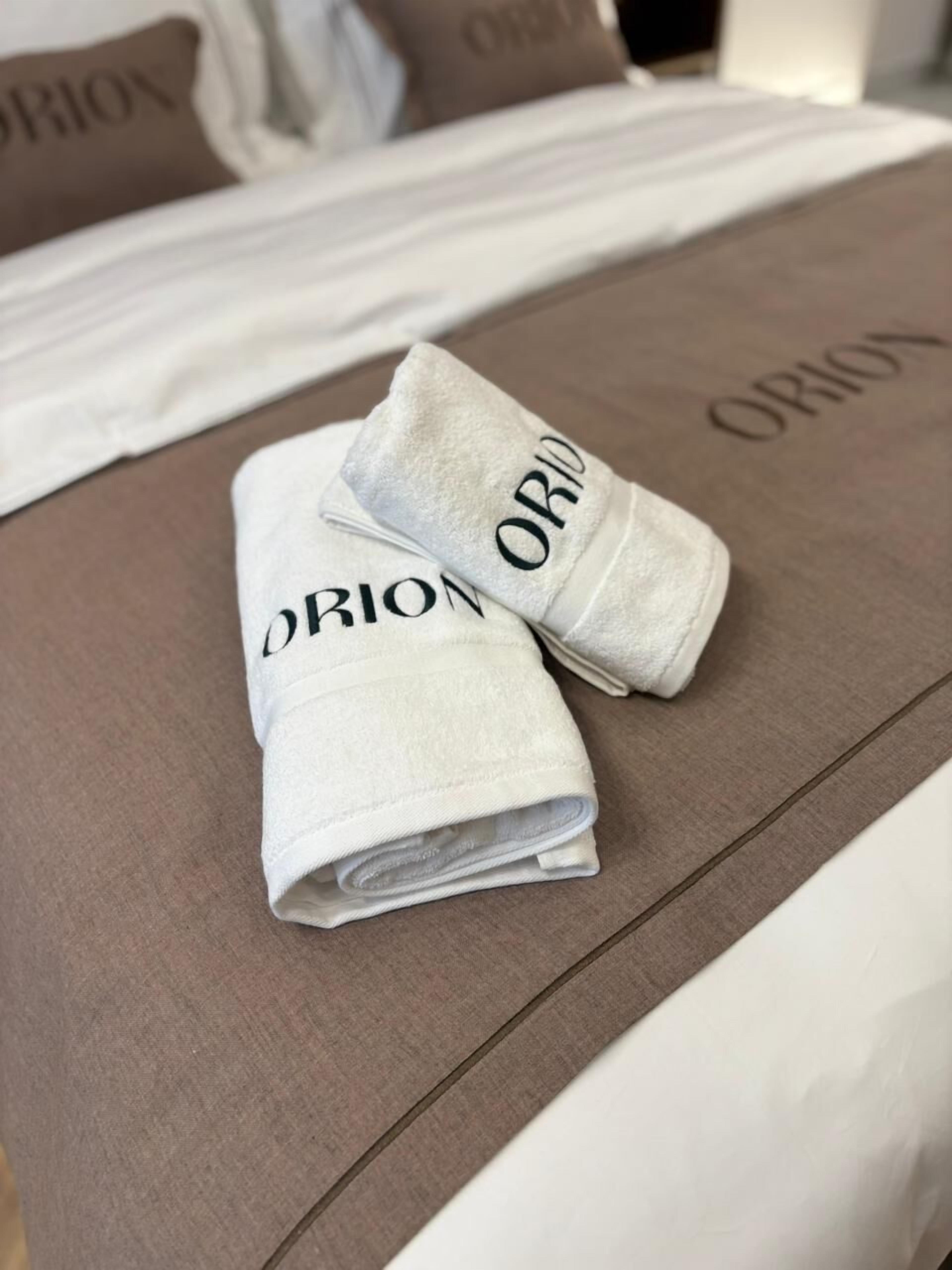A neatly made bed with pillows labeled 'ORION' and a folded towel with the same name.