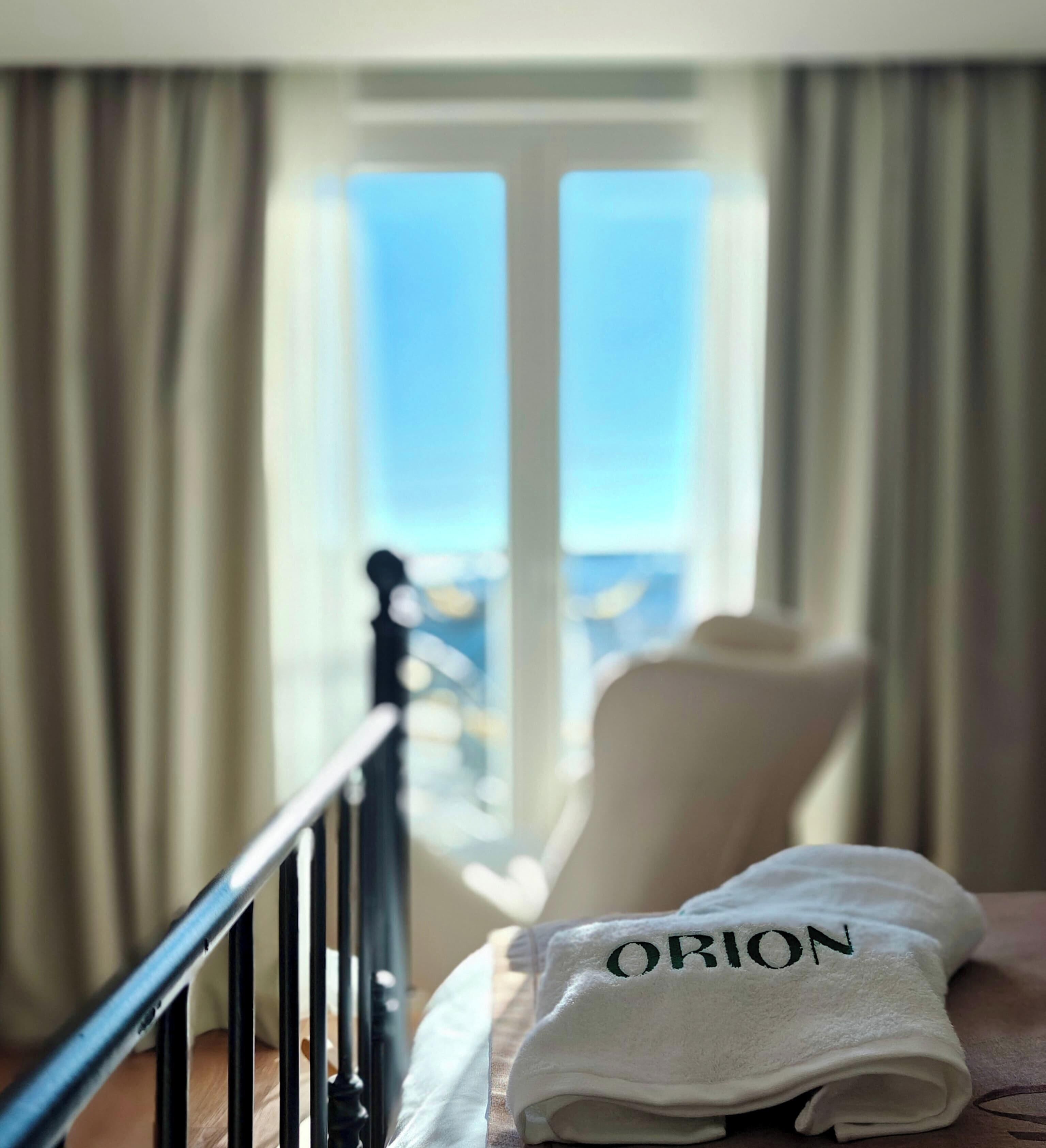 Una habitación de hotel con una cama, un ventanal con cortinas y vista al cielo.