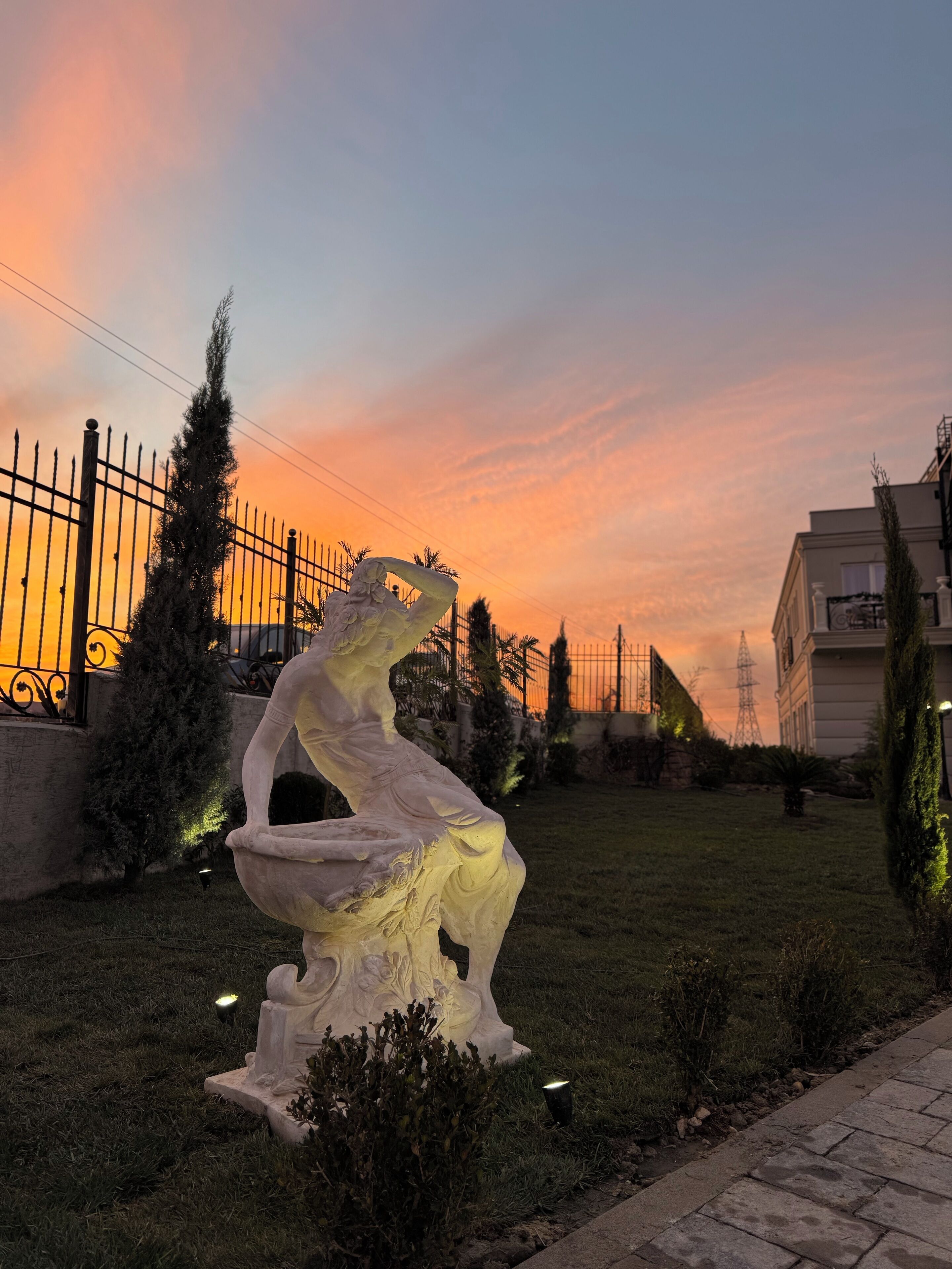 A sculpture of a horse in a garden setting with a sunset in the background.