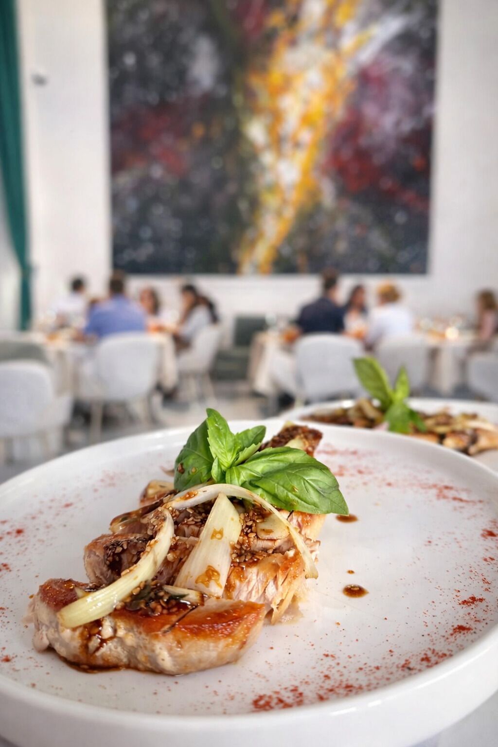 Eine Restaurantszene, wobei ein mit Basilikum garniertes Gericht im Fokus steht.