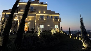 Un edificio de varios pisos con balcones, ventanas iluminadas y un jardín ajardinado con árboles.