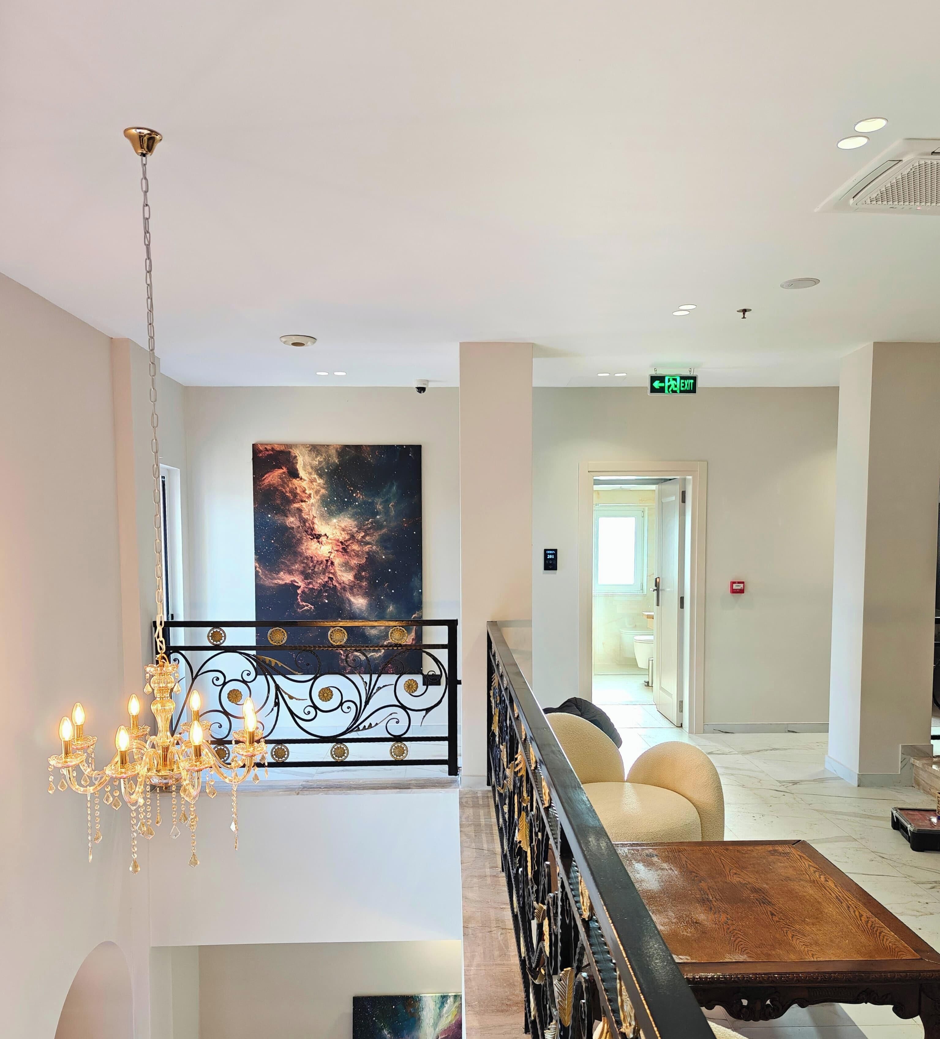 A hotel lobby with a chandelier, a large galaxy-themed painting, a sofa, and a wooden table.