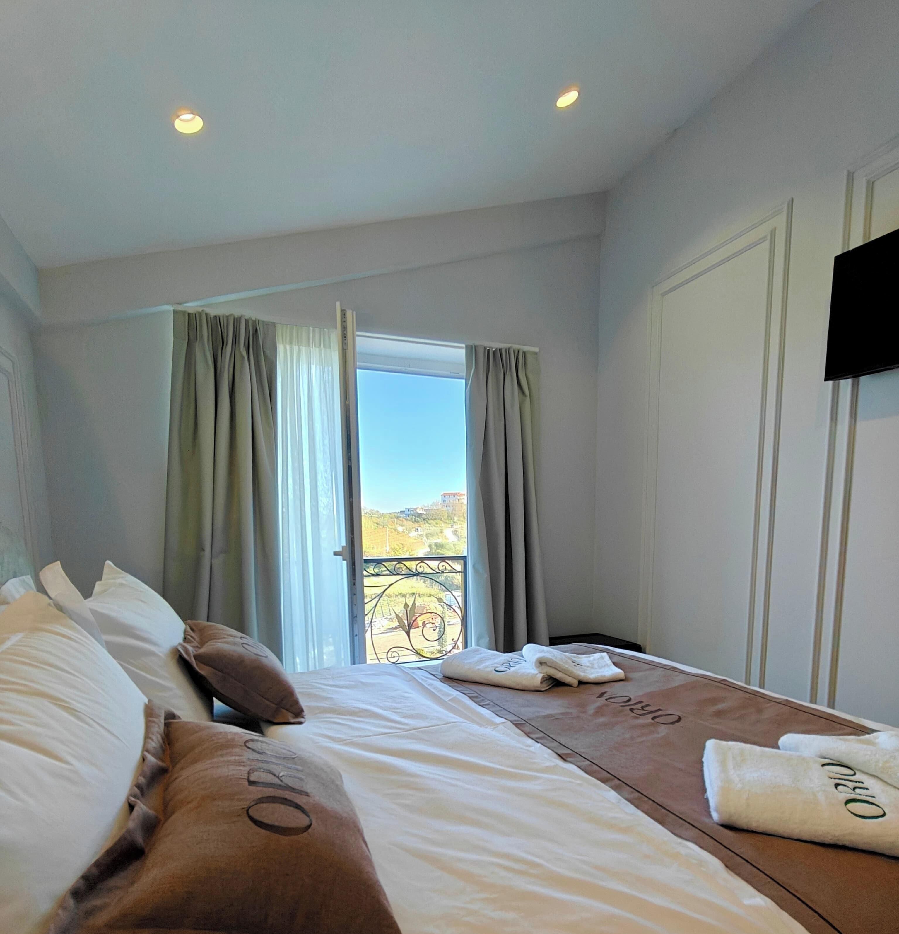 A hotel room with a bed, pillows, a TV, and a window with curtains.
