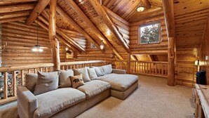 Ein Blockhaushaus-Interieur mit einem großen Ecksofa, Holzbalken und einer Steinwand.
