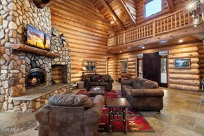 A log cabin interior with a stone fireplace, leather sofas, and a stone wall.