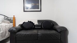 A black leather sofa with two black pillows, a framed picture on the wall, and a bed with white bedding in the background. - Cozy Private 2 bedroom apartment, free Wifi, free parking in heart of Toronto (Toronto)