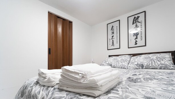 A neatly made bed with a floral-patterned bedspread and pillows, a wooden door, and two framed calligraphy artworks on the wall. - Cozy Private 2 bedroom apartment, free Wifi, free parking in heart of Toronto (Toronto)