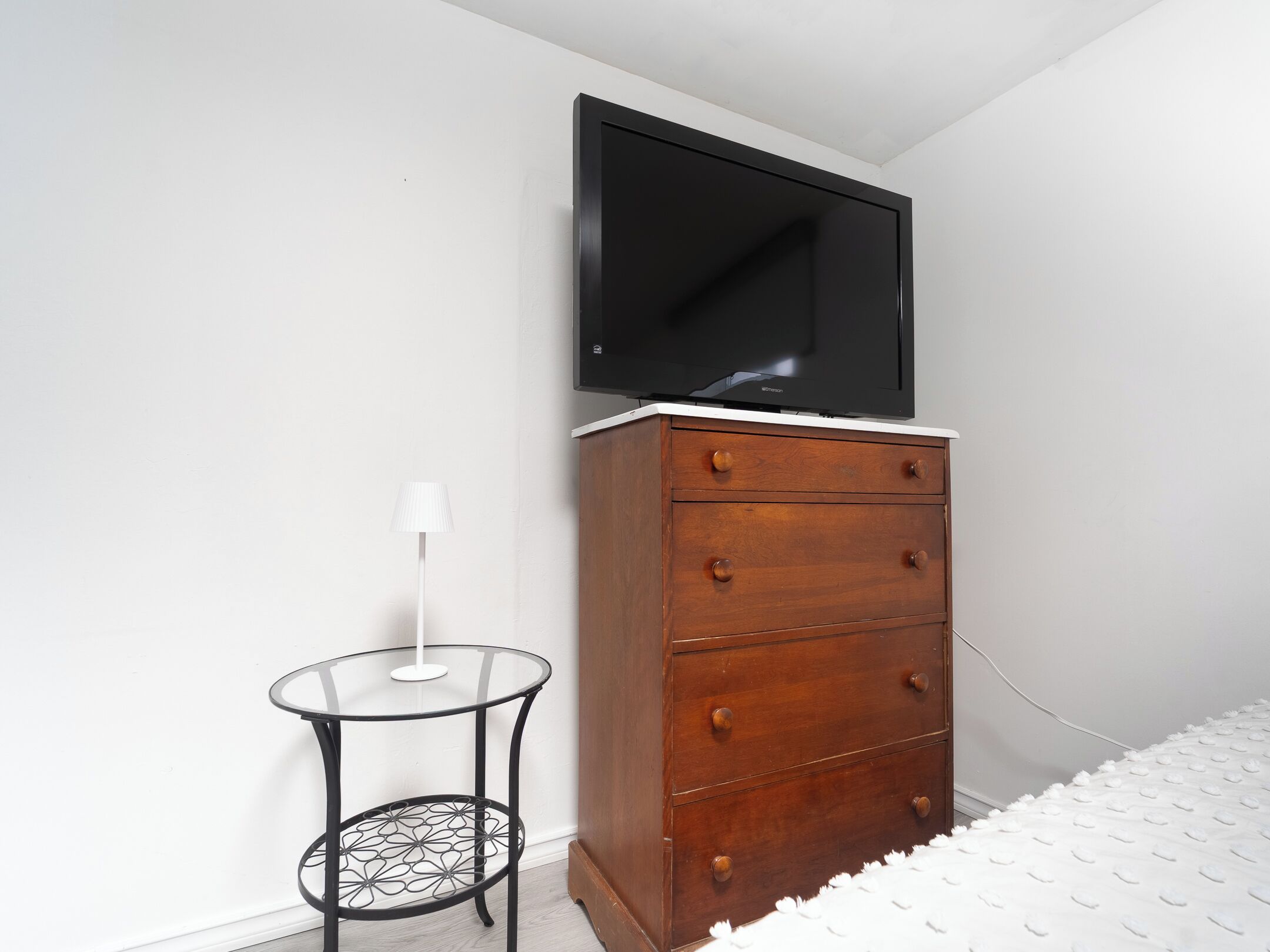 A bedroom with a wooden dresser, a small round table, and a TV mounted on the wall.