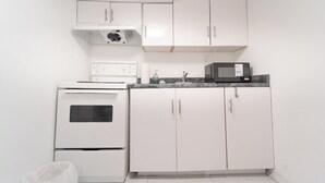A compact kitchen with white cabinets, a microwave, an oven, and a trash bin. - Cozy Private 2 bedroom apartment, free Wifi, free parking in heart of Toronto (Toronto)