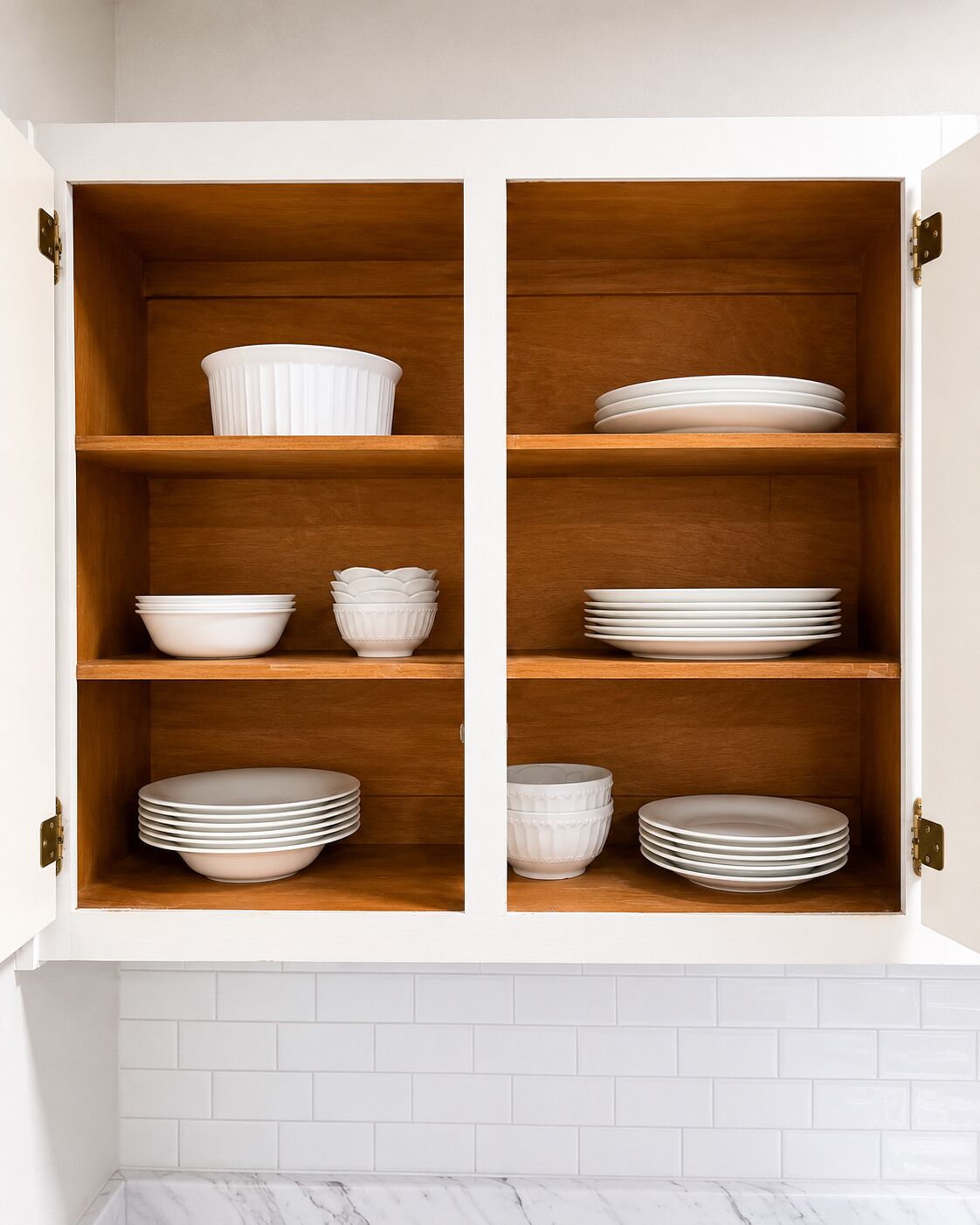 A white cabinet with wooden shelves containing white dishes.