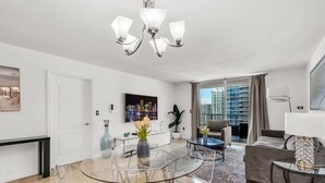 A modern living room with a glass dining table, a sofa, and a city view through large windows. - Stylish 1BR Brickell Retreat Walk to Everything (Miami)