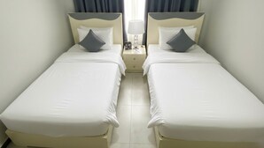 Quarto duplo com duas camas de solteiro, mesa de cabeceira com abajur e janela com cortinas.