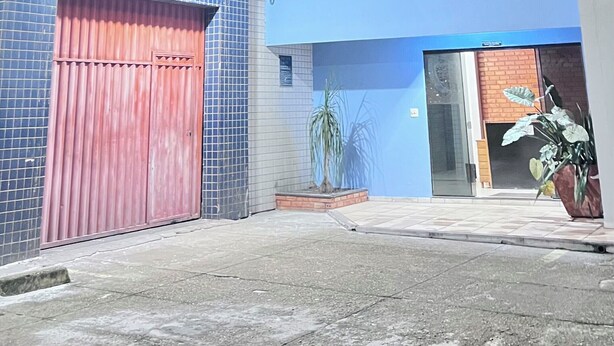A multi-story building with a blue facade, a red garage door, and a potted plant in the foreground. - Braz Hotel (Tomé-Açu)