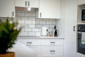 A modern kitchen with white cabinets, a stainless steel range hood, and a tiled backsplash. - Paws and Palms Hideaway in Nelson Bay (Nelson Bay)
