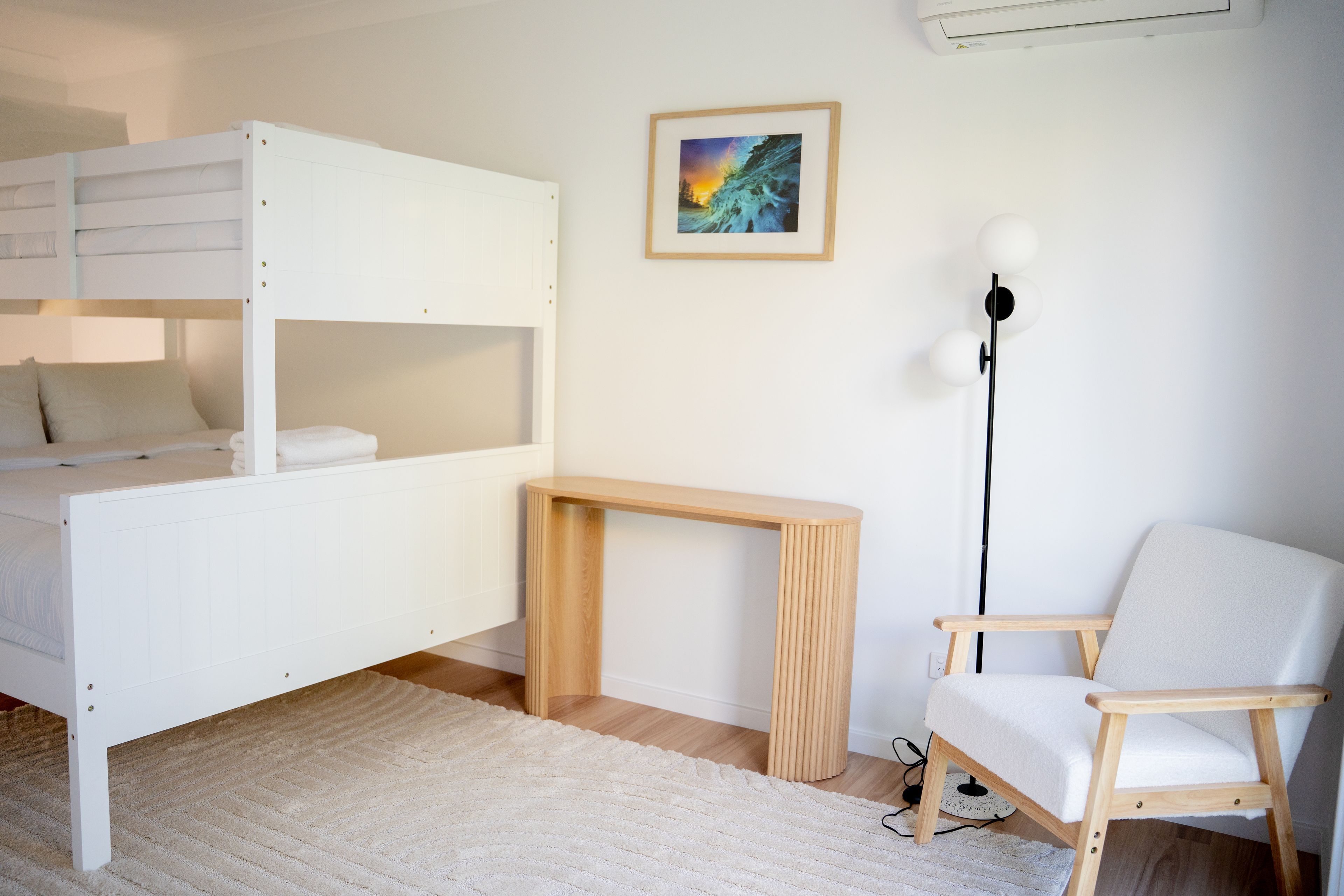 A bedroom with a bunk bed, a bedside table, a chair, a floor lamp, and a framed picture on the wall.