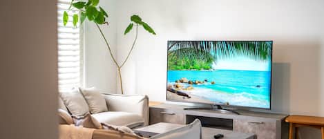 Een woonkamer met een flatscreen televisie op een standaard, een bank, een salontafel en een plant.
