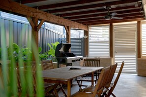 An outdoor patio with a wooden table and chairs, a barbecue grill, and a view of the outside. - Paws and Palms Hideaway in Nelson Bay (Nelson Bay)