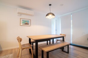 A dining area with a wooden table, chairs, and a bench. There is a ceiling light fixture above the table. - Paws and Palms Hideaway in Nelson Bay (Nelson Bay)