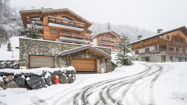 Ein Chalet im Chalet-Stil mit einer Steinfassade und Holzfassade, inklusive einer großen Garage und einem Schild mit der Aufschrift 'Chalet Angelus'.