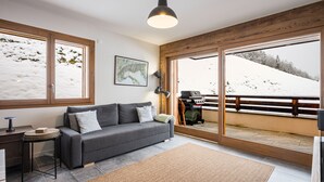 Ein modernes Wohnzimmer mit einem grauen Sofa, einem Couchtisch und einem großen Fenster mit Blick auf eine verschneite Landschaft.