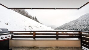 Ein überdachter Außenbereich mit Grill, einer Holzbank und Blick auf eine verschneite Berglandschaft.