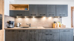 Eine moderne Küche mit grauen Schränken, einem Holzregal, einer Kaffeemaschine und einem Spülbecken.