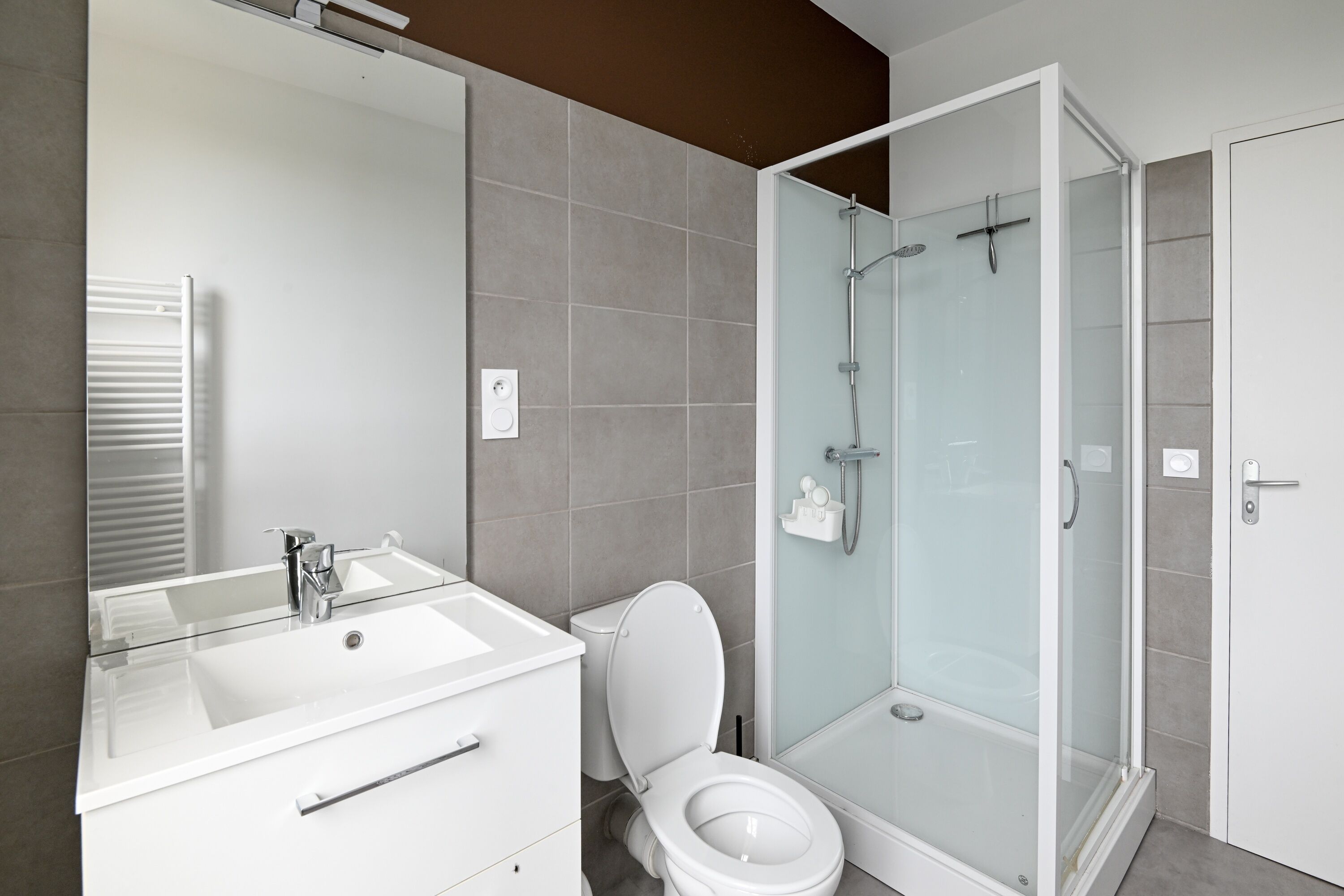 Ein modernes Badezimmer mit einer Glaskabine zur Dusche, einem weißen Waschbecken und einer Toilette.
