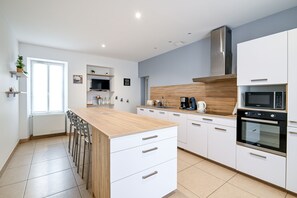 A modern kitchen with white cabinets, a wooden countertop, and a built-in oven. - Gîte de la Poste - Avec jardin (Ryes)