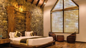 A bedroom with a stone wall, a large window, a bed with pillows, and a wooden headboard. - Corbett Mystic Inn An ExclusiveBoutique  (Ramnagar)