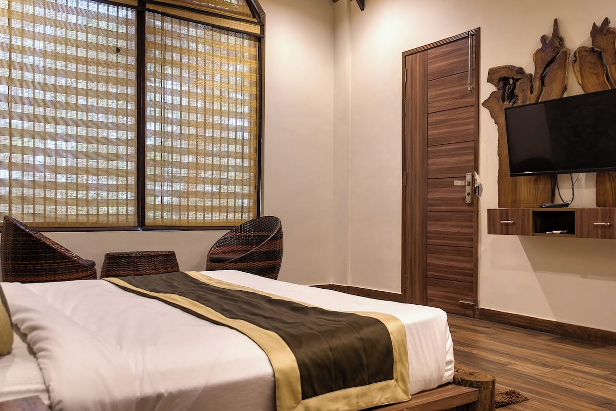 A bedroom with a bed, a television mounted on a wooden panel, and a window with blinds.