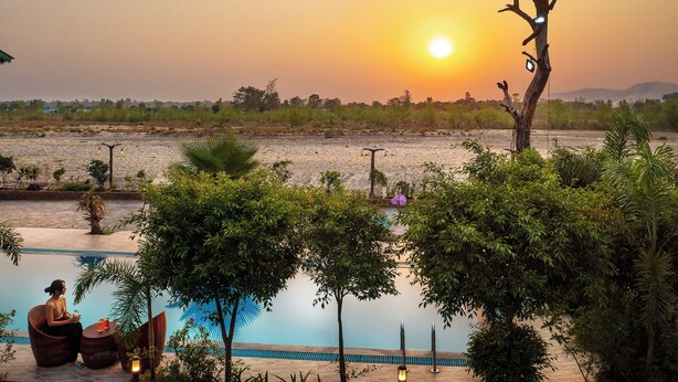 A pool area with a sunset view, surrounded by greenery and a few trees. - Corbett Mystic Inn An ExclusiveBoutique  (Ramnagar)