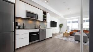 A modern kitchen with built-in appliances, a flat-screen TV, and a grey sofa in the living area.