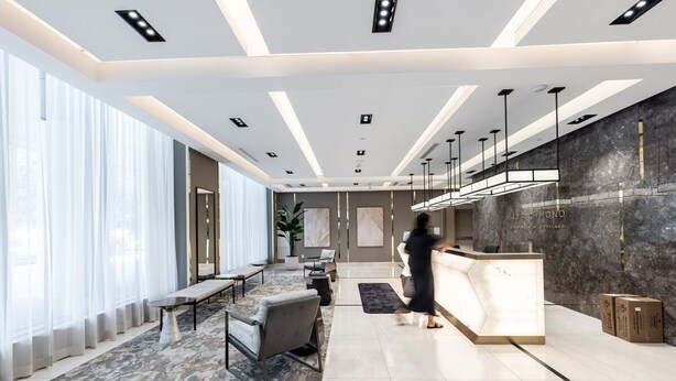 A modern hotel lobby with a reception desk, seating area, and large windows.
