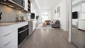 A modern kitchen with white cabinetry, a built-in oven, and a microwave. There is a dining area with a gray sofa and a coffee table.