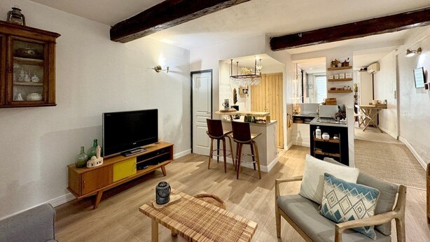 Een woonkamer met een televisie, houten meubels, een eethoek met stoelen en een keuken op de achtergrond.