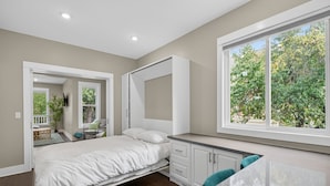 Un dormitorio con cama, escritorio y ventana con vista a árboles.