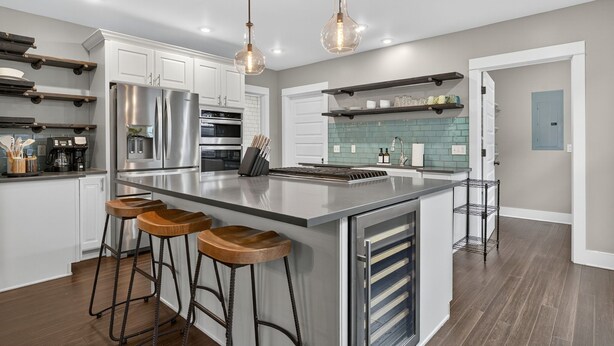 Una cocina moderna con una isla grande, electrodomésticos de acero inoxidable, taburetes de bar de madera e iluminación colgante.