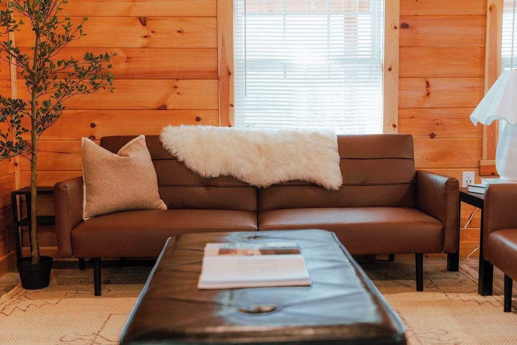 A cozy living room with a brown leather sofa, a white furry throw, and a glass coffee table with a book.